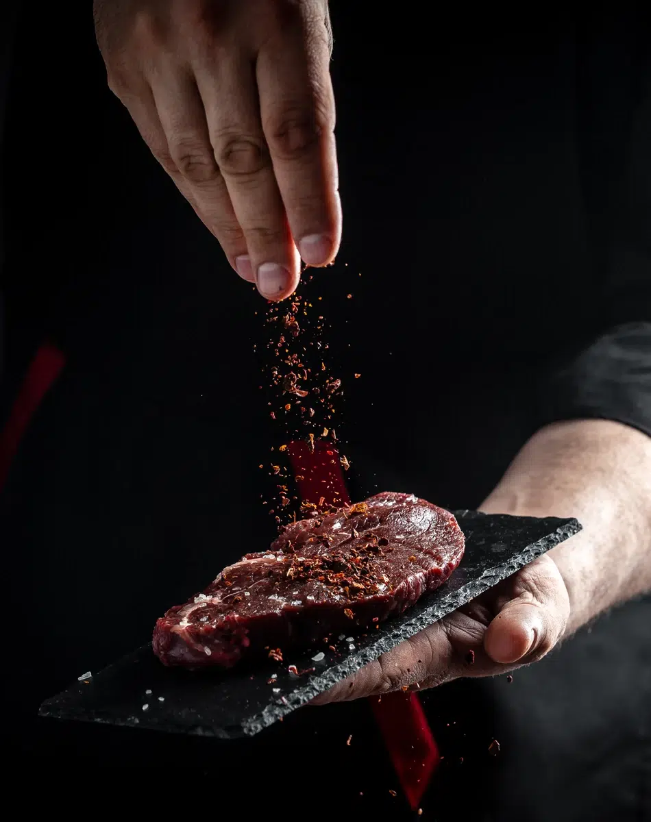 Assaisonnement de steak | LA TABLE DES CLOS Main saupoudrant des épices sur un steak cru